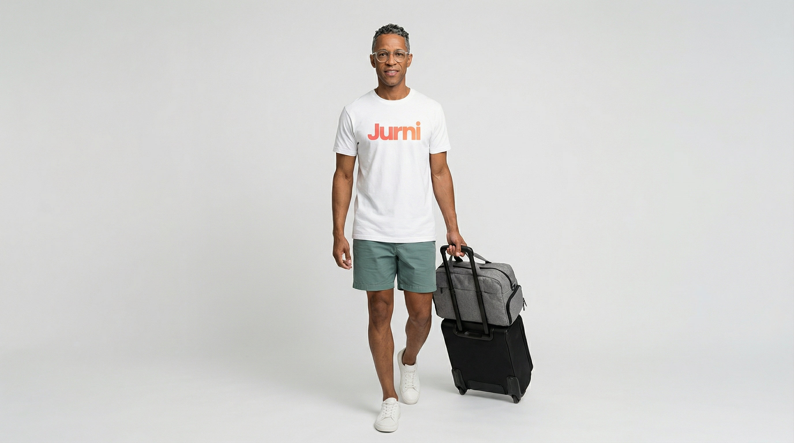 Man carrying black a Jurni travel backpack with rolling luggage, casual travel outfit, white background
